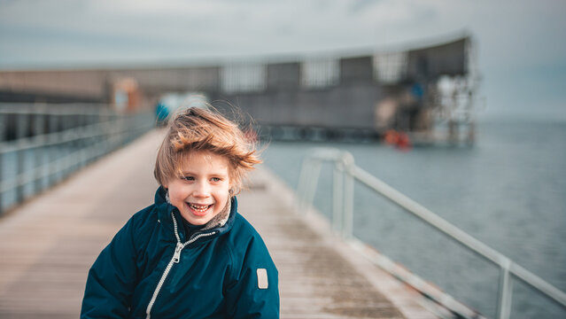 Happy Boy Smiling on Pier, Windblown Hair, Overcast Coastal Scene