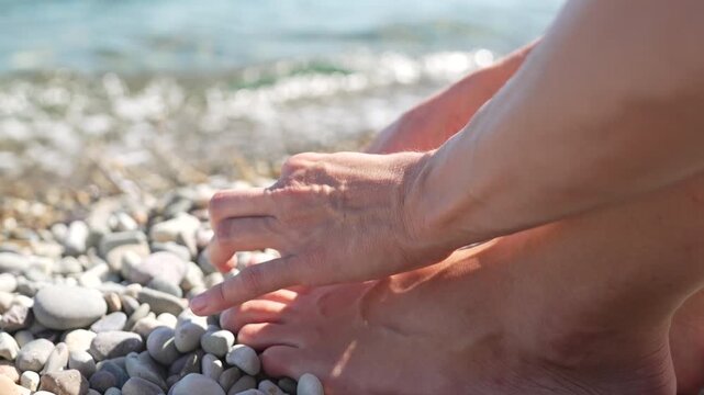 Relaxing foot touch on pebble beach by ocean waves, close up shot. Macro close-up framing action.