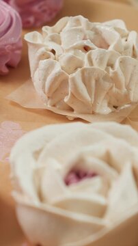 Close up of pink and white rose shaped meringues arranged. Camera smoothly pans to reveal details like ruffled edges. Background features faint floral patterns emphasizing