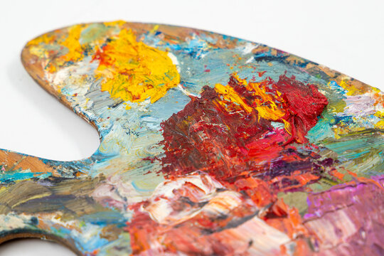 Wooden artist palette with thick oil paint strokes on white background close up. Classic painter tool with messy colorful impasto texturized pigments. Creative art studio backdrop with copy space.