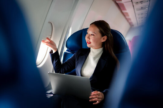 woman uses laptop looks out airplane window enjoying flight contemplating business travel and future success