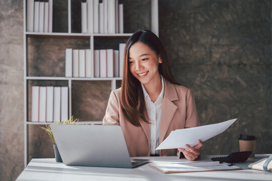Asian Business Woman Smiling While Working on Laptop Holding Doc