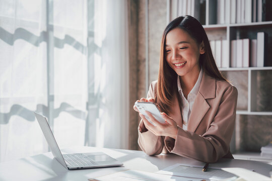 Young Asian Woman Using Smartphone for Business at Desk with Lap