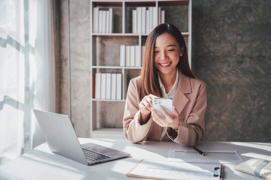 Young Asian Woman Working with Laptop and Mobile Phone at Desk i