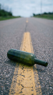 Empty wine bottle lying on highway road asphalt. Danger of driving under influence and drunk driving traffic safety concept. Alcohol abuse and road accident prevention awareness campaign.