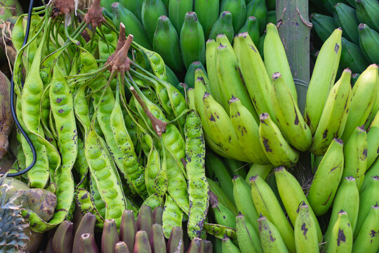 Bunches of fresh green petai pods (stink beans) and unripe green bananas displayed together at a local market stall