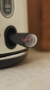 Close up of black cylindrical object with textured end inserted. Red light inside translucent cover illuminates when pressed. White device features 0 1 markings and 0 5L MIN text