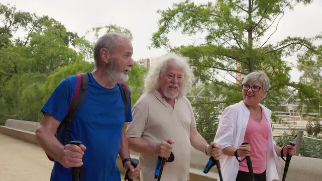 Three happy senior friends enjoying a nordic walk together, chatting and laughing in a city park
