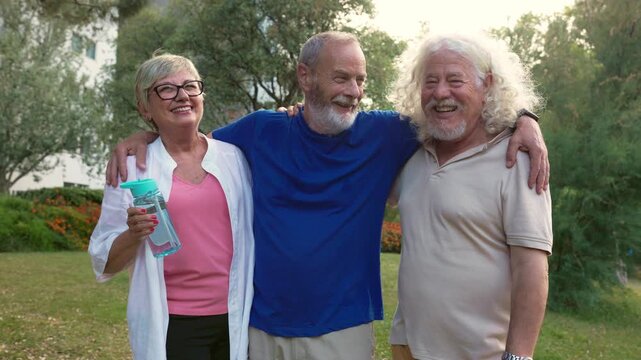 Three happy senior friends hugging, laughing, and chatting in a park after a workout together