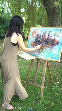 Beautiful woman artist painting on a canvas by the river in a dress