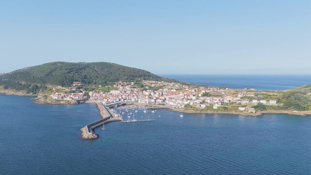 A high-resolution aerial video captures the scenic coastal town of Finisterre in Galicia, Spain. No people are visible in the scene, emphasizing the tranquil and peaceful maritime atmosphere.