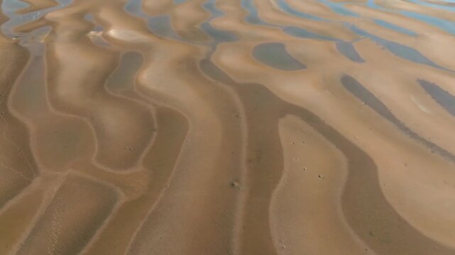 Aerial view of intricate sand ripples and tidal patterns on the beach in Bowen, Queensland, Australia.