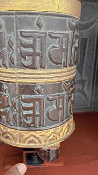 Vertical footage of a traditional Buddhist prayer wheel decorated with the sacred Om Mani Padme Hum mantra and ornamental Buddhist artwork. The close-up captures the detailed religious craftsmanship
