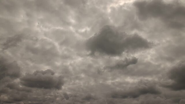 Time-lapse of dense gray clouds moving across daytime sky with sunlight behind overcast cloud cover