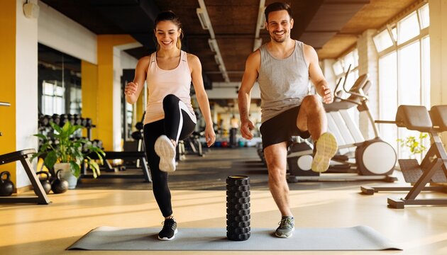 Doing high-knee exercises pair raising knees on mat in gym with foam roller, wearing sport clothes