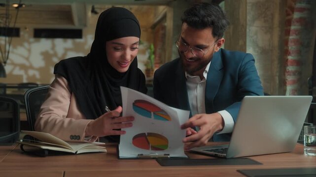 Business team analyze data stats diagram carefree successful company development two Arabian Hindu colleagues in office Muslim businessman businesswoman working rejoice showing thumbs up writing notes