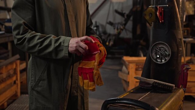 Unrecognizable male welder putting on protective leather gloves in industrial workshop, cropped. Perfect for industrial safety campaigns, manufacturing promotions, and vocational training videos