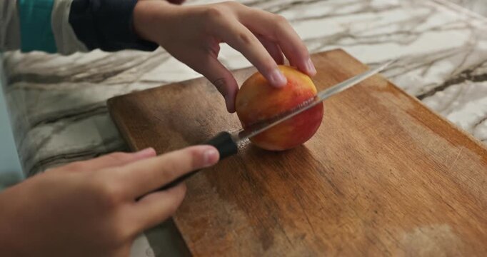 Kid hands cut with knife peach on wooden board. Boy prepare food in kitchen. 4K 10-bit