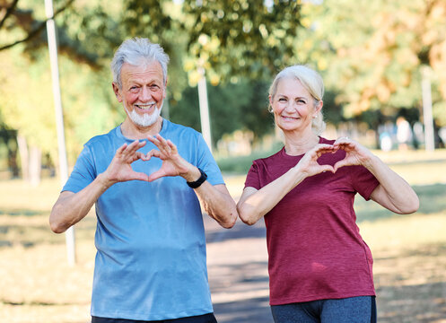 Smiling active mature middle aged couple people posing together forming heart shape with hands  in the park