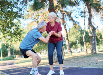 Fototapeta premium Active mid age senior mature couple jogging together, helping and supporting each other with a injury problem in the park