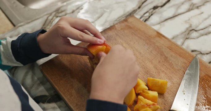 Kid hands cut with knife peach on wooden board. Boy prepare food in kitchen. 4K 10-bit