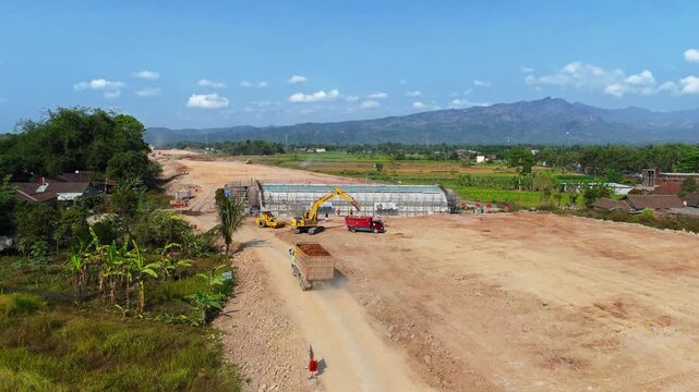 Aerial view of toll road construction site with heavy machinery and earthworks in Muntilan, Central Java, Indonesia.