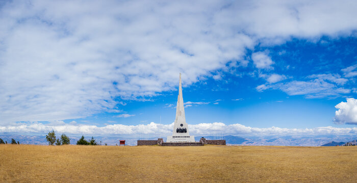 View of the Pampa De La Quinua monument standing in a dry grassy field under a bright blue sky in Quinua, Ayacucho, Peru.