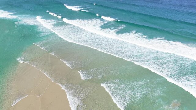 Aerial footage of Praia do Rostro in Galicia, Spain, showing turquoise waves rolling onto a wide sandy beach.
