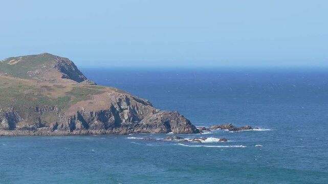 Wide shot of the rugged, rocky coastline at Praia do Rostro in Spain, featuring a grassy headland jutting into the Atlantic Ocean.