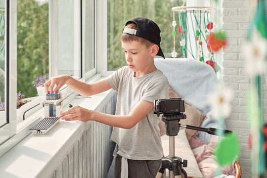 Boy arranges small figurines on a balcony to create a stop motion cartoon, using a camera on a tripod to film his miniature scene. Creative child explores animation, storytelling and filmmaking.