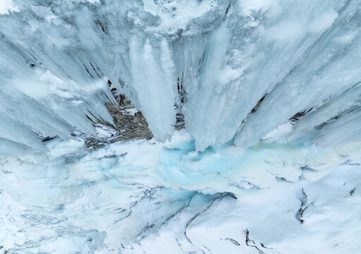 Aerial view of a frozen waterfall with massive icicles hanging over a snow-covered riverbed, showcasing vibrant blue ice textures in Valldal, More og Romsdal, Norway.