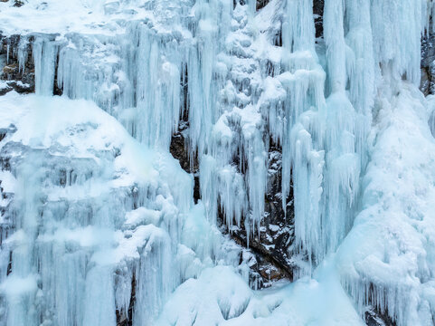 Aerial view of a massive frozen waterfall with intricate icicles and ice formations clinging to a rugged rocky cliff face in winter in Valldal, More og Romsdal, Norway.