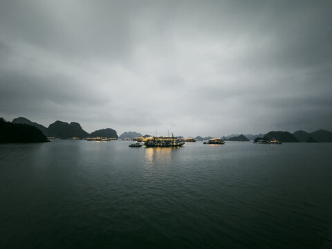 View of cruise boats anchored in Ha Long Bay with limestone karsts under an overcast sky in Vietnam.