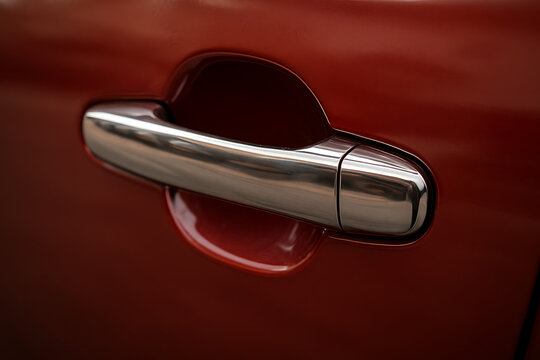 Close-up of a chrome car door handle on glossy red vehicle body