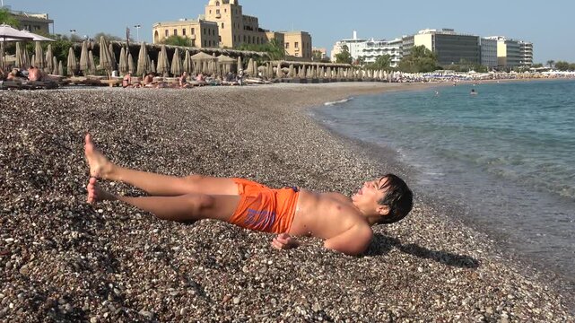 Rhodes Town, Greece - 23 ofOctober 2023: Chubby boy walking out of the sea and falling on the beach
