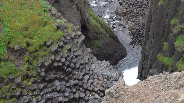 Rugged volcanic landscape with river flowing through rocky canyon and natural cave formations in Iceland. Dramatic scene of basalt rocks