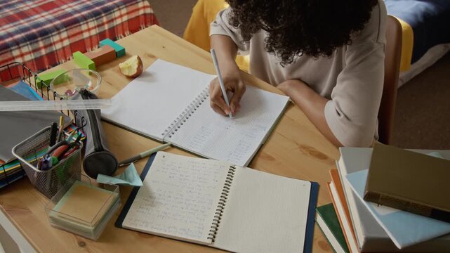 African American teenage boy writing math equations in notebook during study session, high angle view. Video is perfect for online learning platforms and school supply marketing campaigns
