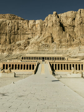 View of the Mortuary Temple of Hatshepsut with its iconic colonnades and stone ramps set against the dramatic limestone cliffs of Deir el-Bahari, Egypt.
