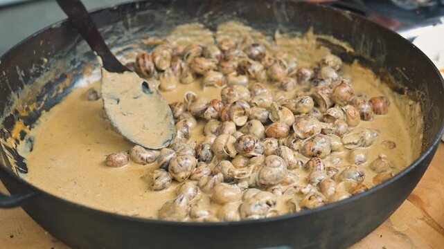 Snails in sauce are cooked in a large frying pan.