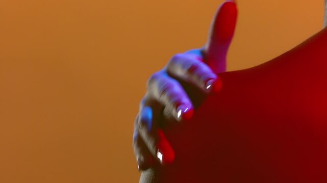 Big close-up shot of female model lit with blue and red lighting standing back to camera stroking her nape and shoulder with orange backdrop | Luxury fragrance footage