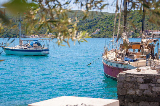 Two boats anchored in a calm blue sea near a rocky shore. Lush green hills are visible in the background under a clear sky.