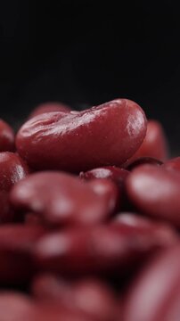 Pile of boiled red kidney beans with steam rising, slowly rotating on a black background.