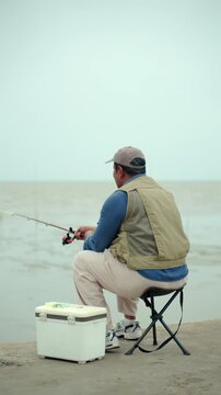 Happy senior man sitting by the sea and fishing with a rod after retirement. Active aging, healthy longevity, outdoor leisure, fulfilling retirement. Life insurance and financial security concept.
