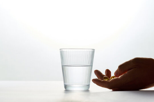 Person Holding Vitamin Capsules Next to Glass of Water