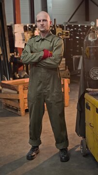 Portrait of young adult Caucasian man wearing overalls and protective gloves, crossing arms in welding workshop. Footage is ideal for industrial recruitment and trade school ads, vertical