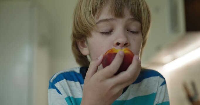 Caucasian kid boy enjoy eating peach in kitchen. 4K 10-bit
