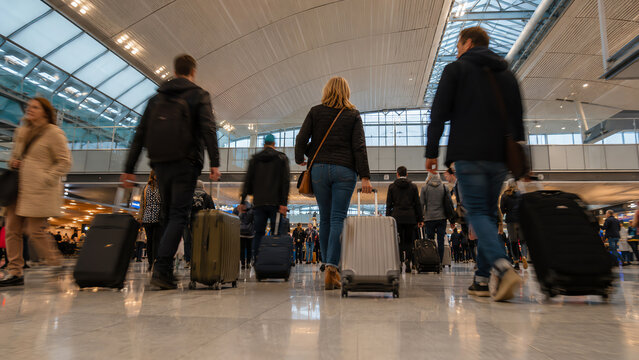 Travelers walk through a busy airport terminal with luggage, showcasing the energy and diversity of modern travel experiences.