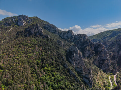 Aerial view of the rugged cliffs of Belvedere du Diable near Gorges de la Pierre-Lys, featuring dense Pyrenees forests and the winding L'Aude river in Belvianes-et-Cavirac, Occitanie, France.