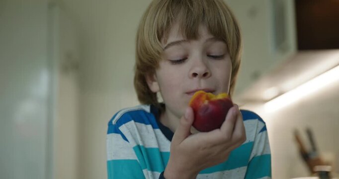 Caucasian kid boy enjoy eating peach in kitchen. 4K 10-bit