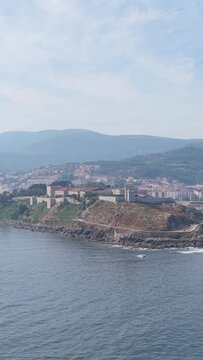 Vertical 9:16 aerial video showing Castelo de Monterreal, a historic fortress on a rocky peninsula overlooking the Atlantic Ocean in Baiona, Galicia, Spain. No people are visible in the frame.